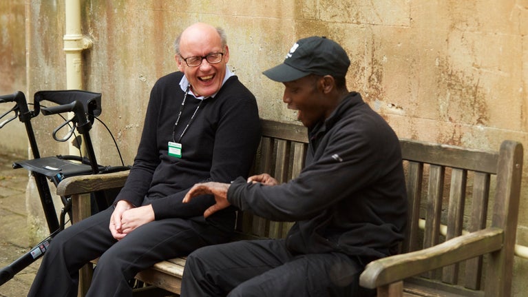 Two male volunteers sit on a bench, chatting and laughing
